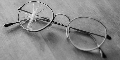 A pair of glasses with a cracked lens on a wood surface